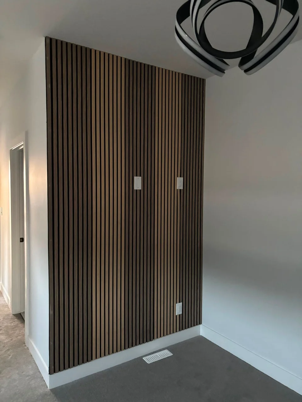 Floor-to-ceiling wood-toned slatted feature wall beside white walls