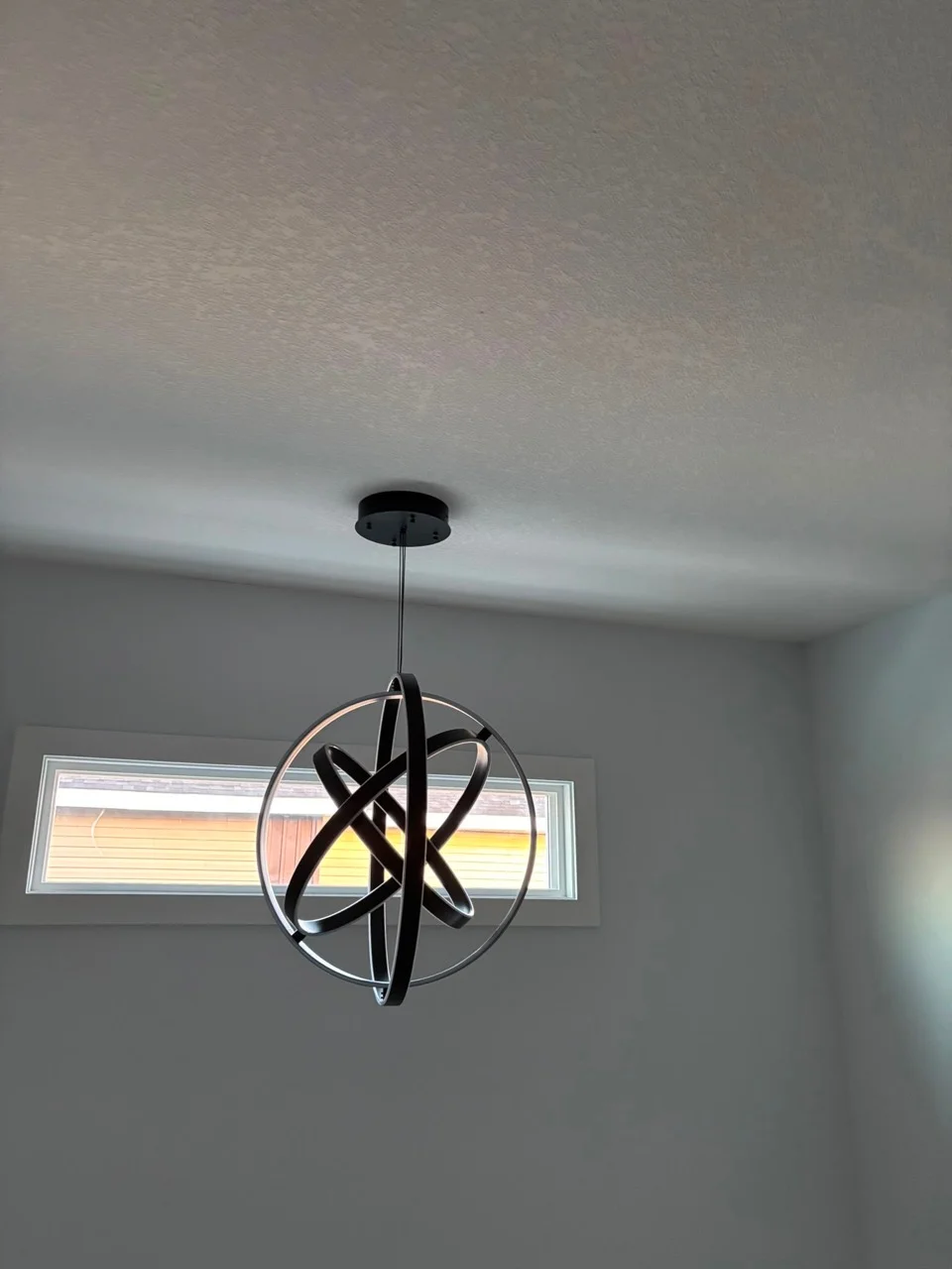 Black interlocking ring pendant light in a pale room with a high horizontal window